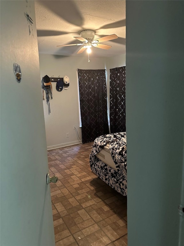 bedroom featuring a textured ceiling, baseboards, brick floor, and a ceiling fan