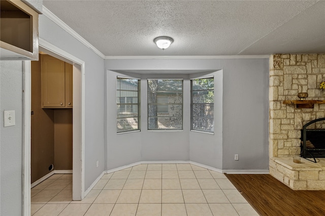 unfurnished dining area with a fireplace, a textured ceiling, light wood-type flooring, and crown molding