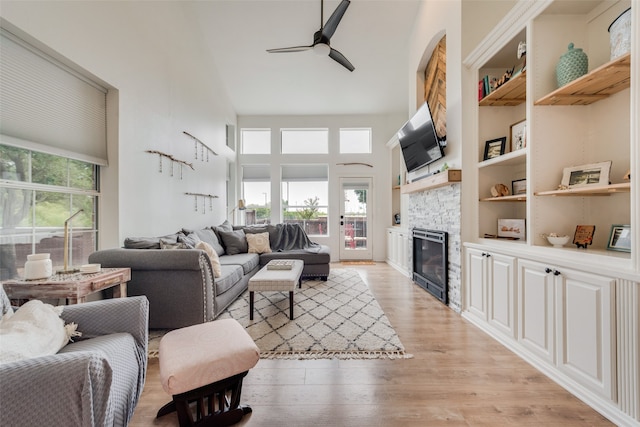 living room featuring a high ceiling, ceiling fan, light hardwood / wood-style floors, and a stone fireplace