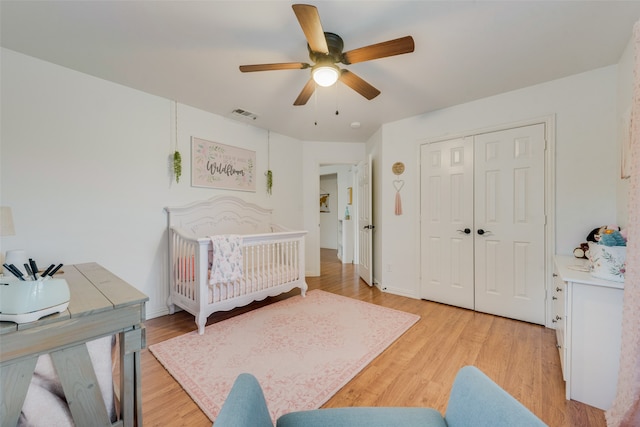 bedroom with a crib, light hardwood / wood-style flooring, ceiling fan, and a closet