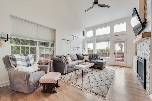 living room with light wood-type flooring, wine cooler, a stone fireplace, ceiling fan, and a towering ceiling