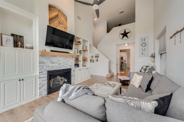 living room with light hardwood / wood-style floors, ceiling fan, a towering ceiling, and a fireplace