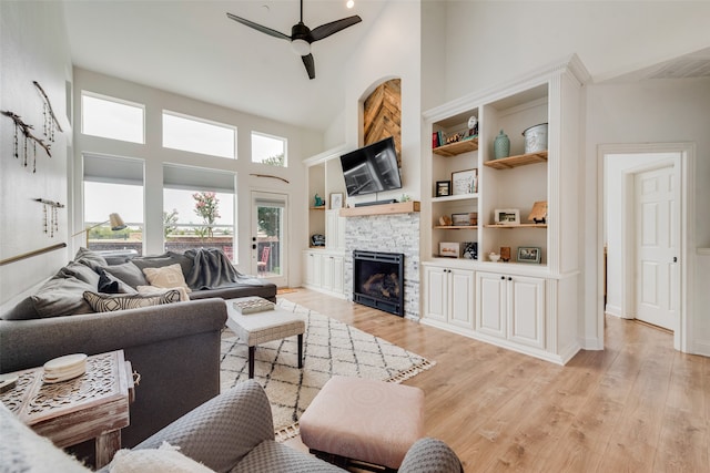 living room featuring light wood-type flooring, ceiling fan, a fireplace, and a high ceiling