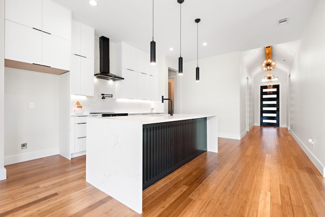 kitchen with pendant lighting, light hardwood / wood-style flooring, wall chimney exhaust hood, a center island with sink, and white cabinets