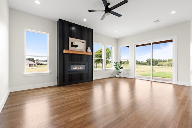 unfurnished living room featuring a large fireplace, ceiling fan, a wealth of natural light, and wood-type flooring