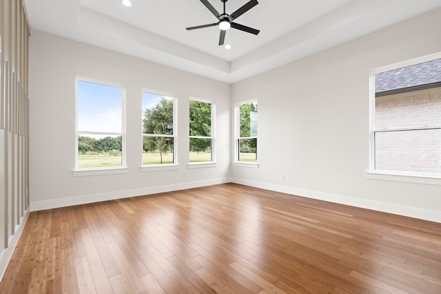 unfurnished room with light wood-type flooring, a tray ceiling, and ceiling fan