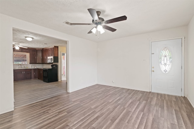 interior space with a textured ceiling, ceiling fan, sink, and light hardwood / wood-style floors