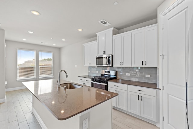 kitchen featuring a center island with sink, appliances with stainless steel finishes, sink, dark stone countertops, and white cabinets