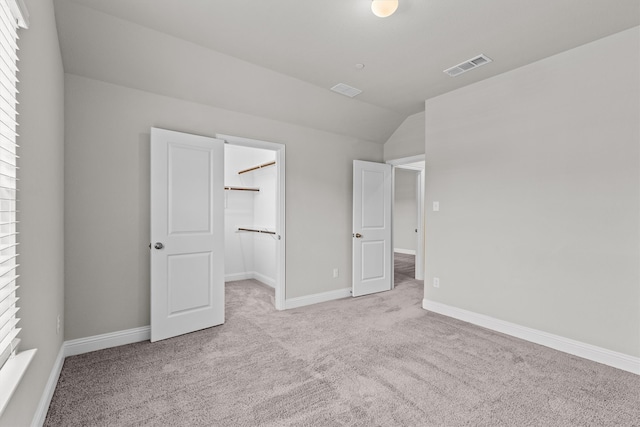 unfurnished bedroom featuring light carpet, vaulted ceiling, a spacious closet, and a closet