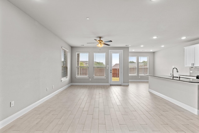 unfurnished living room with ceiling fan, sink, and light hardwood / wood-style floors