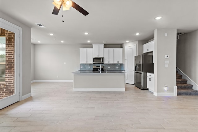 kitchen featuring white cabinets, stainless steel appliances, ceiling fan, a center island with sink, and tasteful backsplash