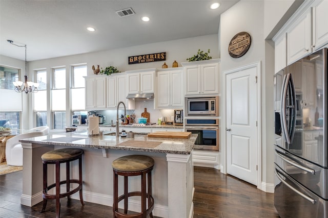 kitchen with white cabinets, light stone counters, dark hardwood / wood-style floors, pendant lighting, and stainless steel appliances