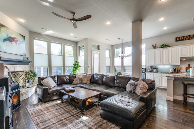 living room with dark wood-type flooring, a healthy amount of sunlight, a textured ceiling, and ceiling fan with notable chandelier