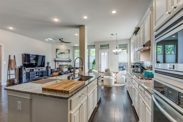 kitchen with appliances with stainless steel finishes, sink, an island with sink, hanging light fixtures, and dark wood-type flooring