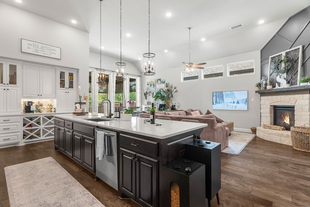 kitchen featuring ceiling fan with notable chandelier, an island with sink, sink, a stone fireplace, and stainless steel dishwasher