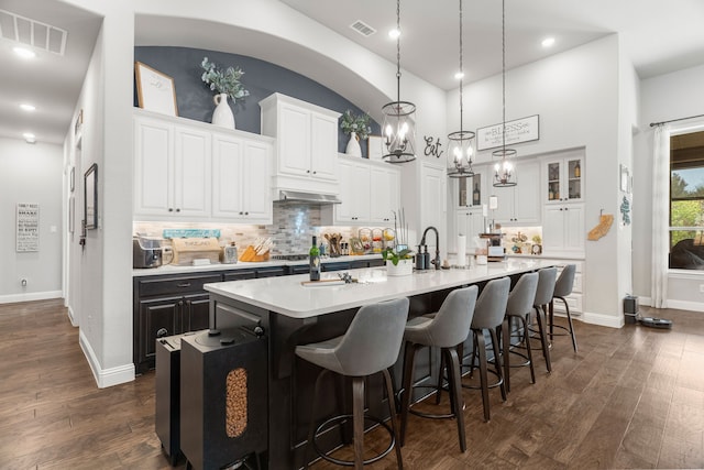 kitchen with an inviting chandelier, white cabinetry, dark hardwood / wood-style floors, an island with sink, and pendant lighting