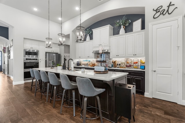 kitchen featuring white cabinets, decorative light fixtures, stainless steel appliances, dark hardwood / wood-style floors, and an island with sink