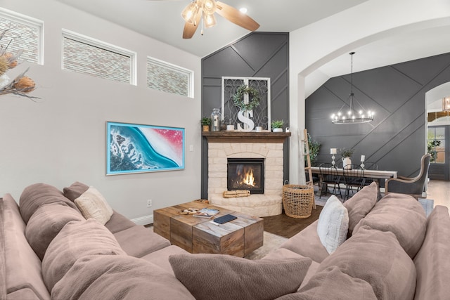 living room with ceiling fan with notable chandelier, a stone fireplace, high vaulted ceiling, and hardwood / wood-style flooring