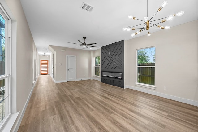 unfurnished living room with ceiling fan with notable chandelier and light hardwood / wood-style floors