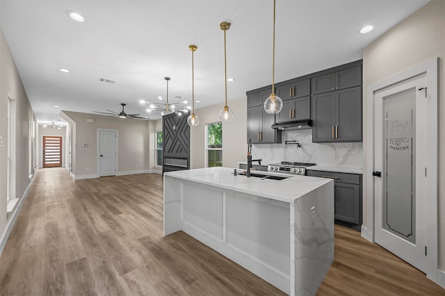 kitchen with pendant lighting, a center island with sink, light wood-type flooring, and tasteful backsplash