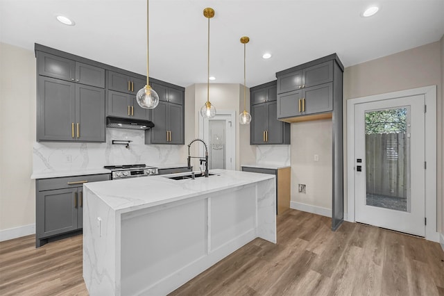 kitchen with a center island with sink, light stone countertops, decorative light fixtures, and sink