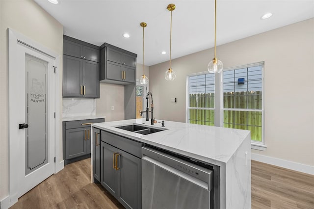 kitchen with a kitchen island with sink, decorative light fixtures, light stone counters, sink, and stainless steel dishwasher