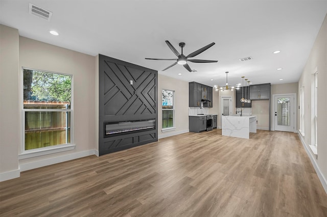 unfurnished living room featuring ceiling fan with notable chandelier, hardwood / wood-style floors, and sink