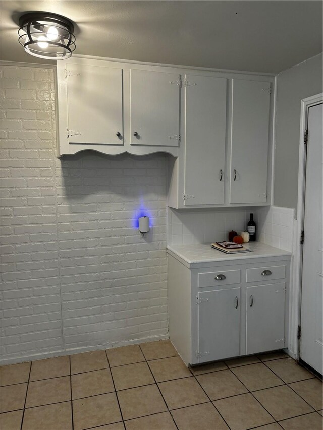 kitchen featuring white cabinetry, brick wall, light tile patterned floors, and decorative backsplash