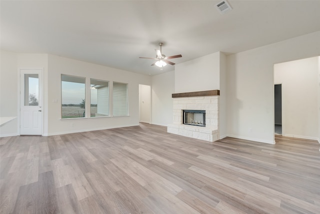 unfurnished living room with light wood-type flooring, a stone fireplace, and ceiling fan