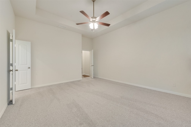 empty room with ceiling fan, light carpet, and a tray ceiling