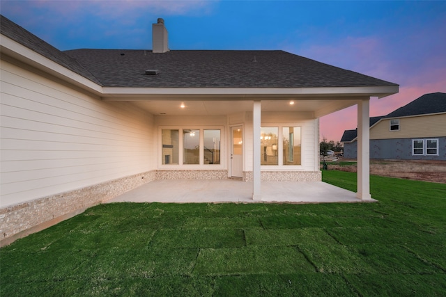 back house at dusk with a lawn and a patio area