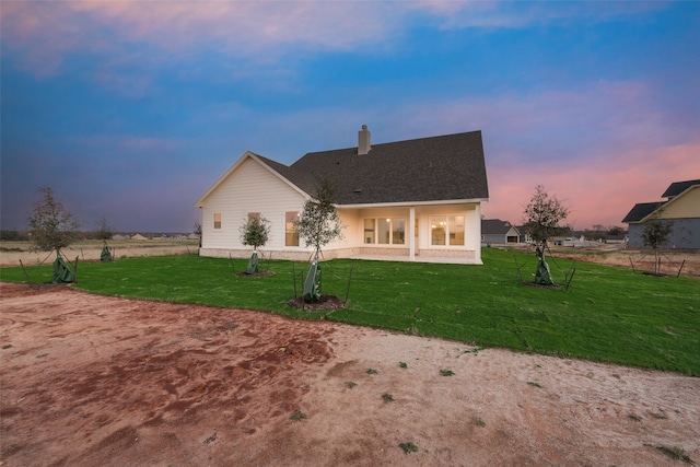 back house at dusk featuring a lawn