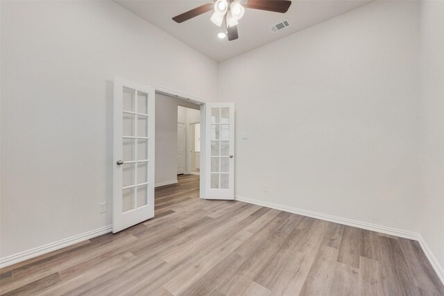 empty room with ceiling fan, french doors, a towering ceiling, and light hardwood / wood-style flooring