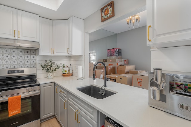 kitchen featuring stainless steel range with electric cooktop, white cabinets, sink, decorative light fixtures, and a chandelier