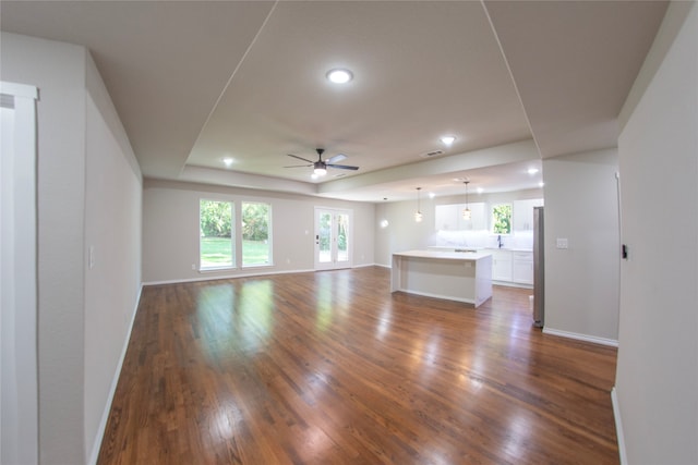 unfurnished living room featuring a healthy amount of sunlight, a tray ceiling, dark hardwood / wood-style flooring, and ceiling fan