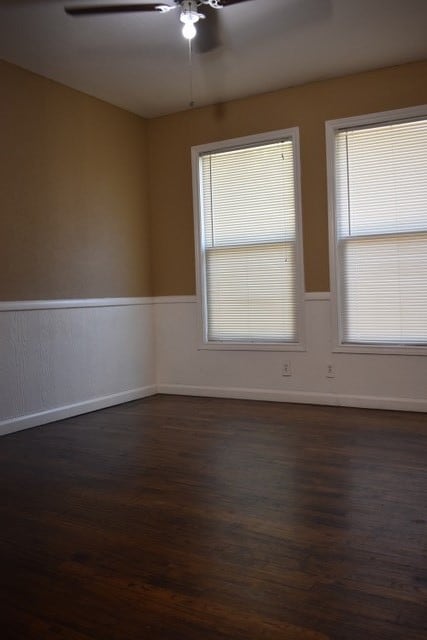 empty room featuring a healthy amount of sunlight, ceiling fan, and dark wood-type flooring