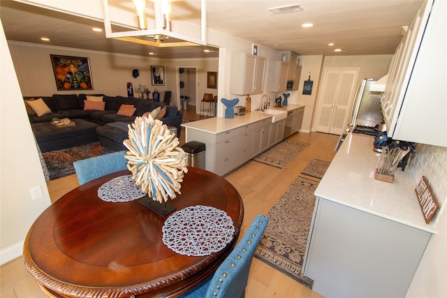 dining space featuring light wood-type flooring, ornamental molding, and sink