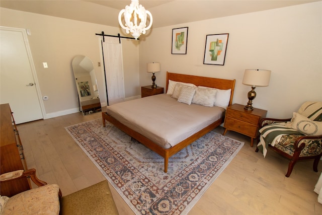 bedroom featuring a barn door, a notable chandelier, and light hardwood / wood-style flooring