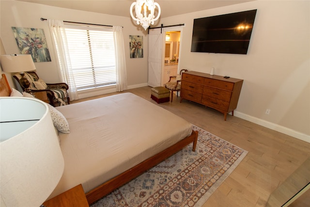 bedroom featuring a barn door, light wood-type flooring, and connected bathroom