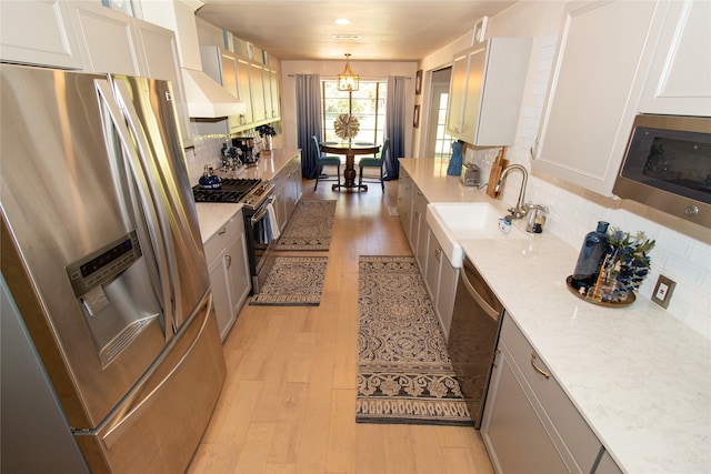 kitchen with light wood-type flooring, appliances with stainless steel finishes, custom range hood, and backsplash