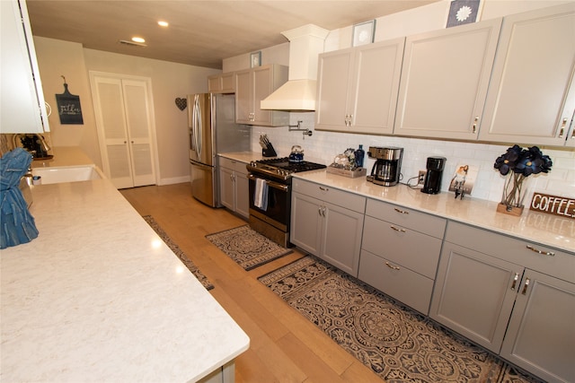 kitchen featuring gray cabinets, hardwood / wood-style floors, appliances with stainless steel finishes, and wall chimney range hood