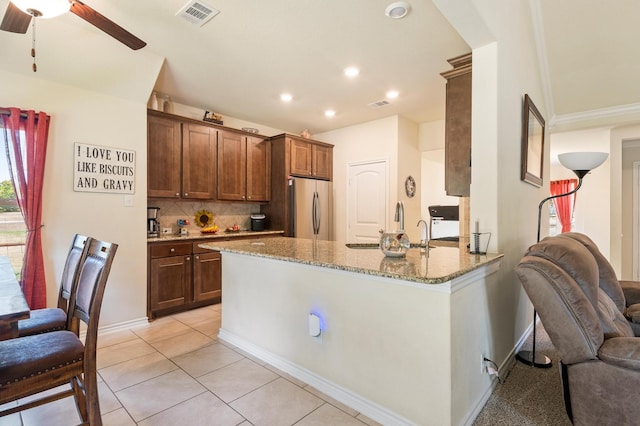 kitchen featuring ceiling fan, light tile patterned floors, kitchen peninsula, stainless steel refrigerator, and light stone countertops