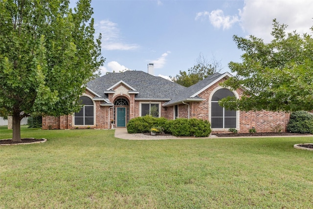 view of front of house featuring a shingled roof, a front lawn, brick siding, and a chimney