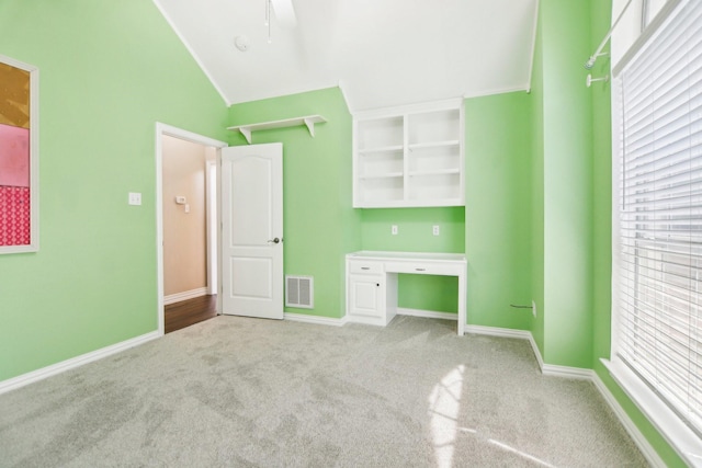 unfurnished bedroom featuring vaulted ceiling, built in desk, carpet floors, baseboards, and visible vents