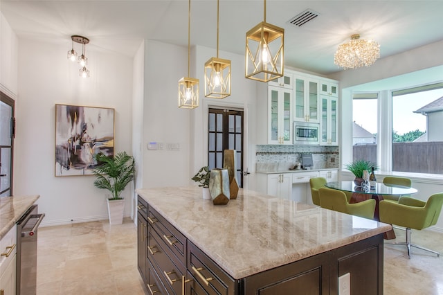 kitchen featuring an inviting chandelier, pendant lighting, decorative backsplash, white cabinets, and appliances with stainless steel finishes