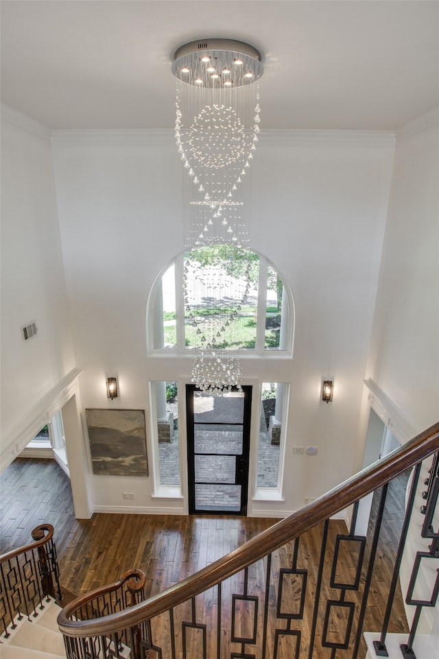 foyer featuring ornamental molding, a towering ceiling, dark wood-type flooring, and an inviting chandelier