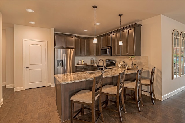 kitchen featuring sink, hanging light fixtures, stainless steel appliances, light stone counters, and dark hardwood / wood-style flooring