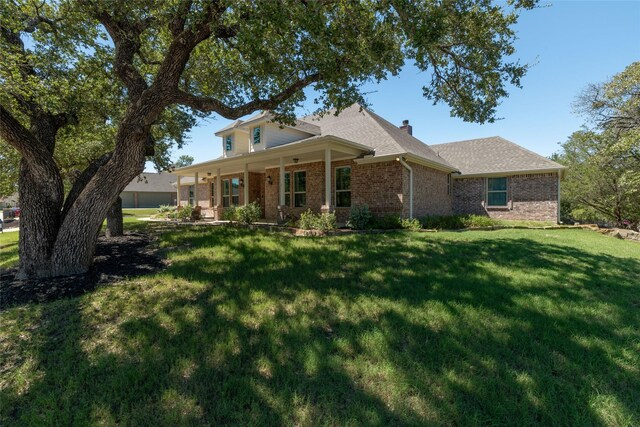 view of front of home with a shingled roof, a front yard, brick siding, and a chimney