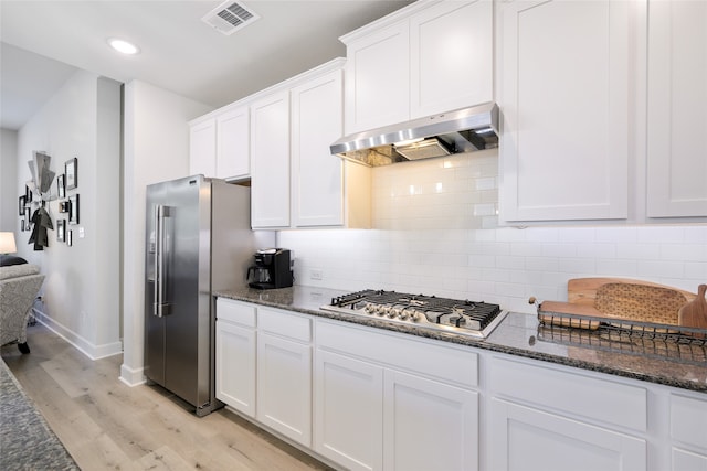 kitchen featuring dark stone counters, appliances with stainless steel finishes, light hardwood / wood-style floors, and white cabinetry