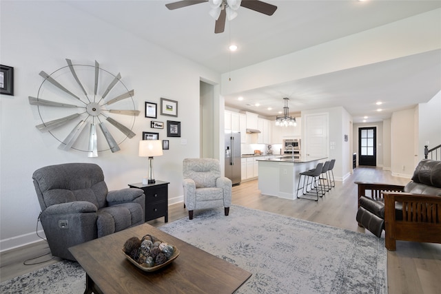 living room with sink, ceiling fan with notable chandelier, and light hardwood / wood-style floors